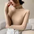 Beige ribbed cashmere turtleneck sweater with a slim fit, high collar, and long sleeves, styled casually with white jeans.