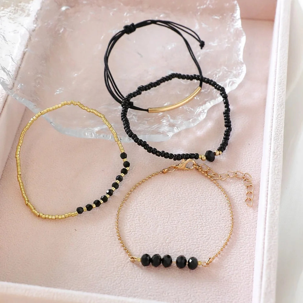 Four-piece bracelet set featuring gold-tone and black onyx glass stones, arranged on a pink display tray.