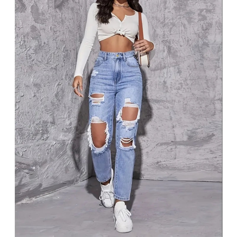 High-waisted distressed straight-leg denim jeans in light blue, featuring large rips and raw edges, paired with a cropped top.
