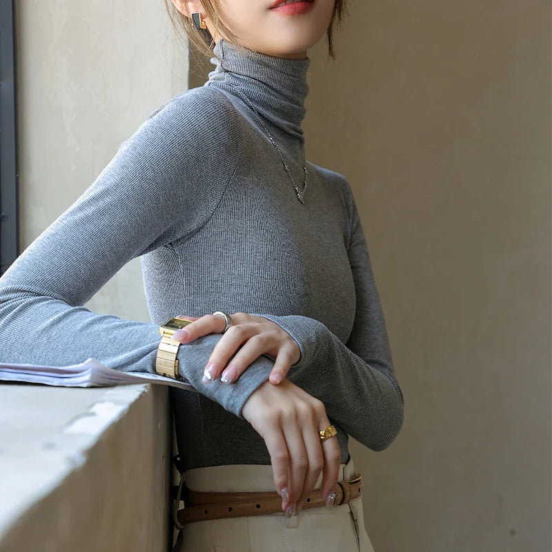 Slim-fit gray ribbed mock-neck pullover with long sleeves, worn casually, featuring a soft texture and elegant silhouette.