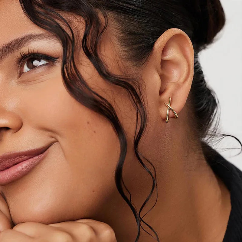 Gold minimalist cross stud earrings worn on the model's ear, showcasing a high-polish finish and delicate design.