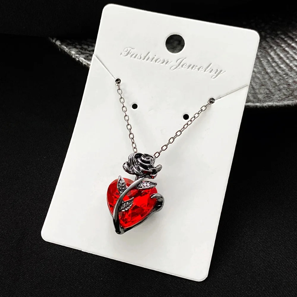 Gothic rose pendant necklace featuring a textured crimson heart wrapped in dark floral metalwork on a silver chain.