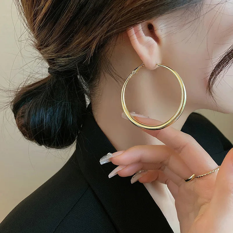 Gold chunky hoop earrings displayed on a model with a low bun, accentuating their high-gloss finish and minimalist design.