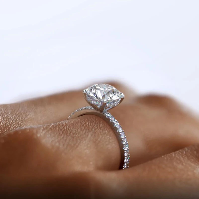 A sparkling 2-carat round-cut Moissanite solitaire ring with a six-prong setting, featuring a silver band adorned with smaller stones.