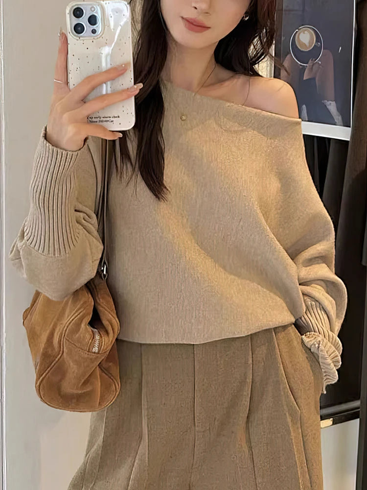 Off-shoulder beige knit pullover with batwing sleeves and ribbed cuffs, styled with a light brown handbag.