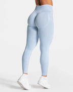 High-waisted light blue seamless leggings with contouring panels, worn with white sneakers and ribbed cuffs.