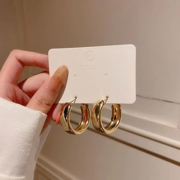 Gold chunky minimalist hoop earrings displayed on a card, held by a hand with a light sweater.