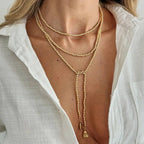 Layered gold pearl necklace with a dropped heart pendant, worn over a white button-up shirt, creating a chic look.