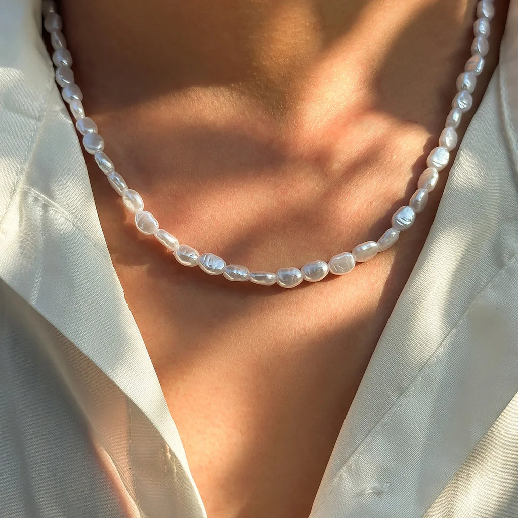 Unisex necklace featuring irregular oval pearls with a glossy finish, worn against bare skin and a light blouse.
