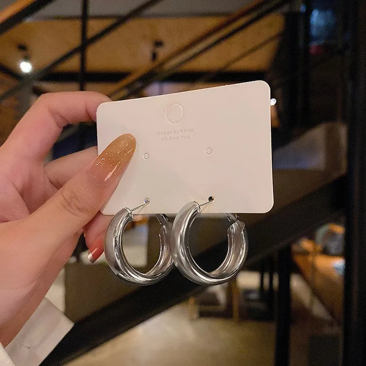 Chunky minimalist hoop earrings with a high-gloss polished finish, displayed on a white card, held by a hand.