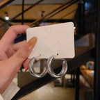 Chunky minimalist hoop earrings with a high-gloss polished finish, displayed on a white card, held by a hand.