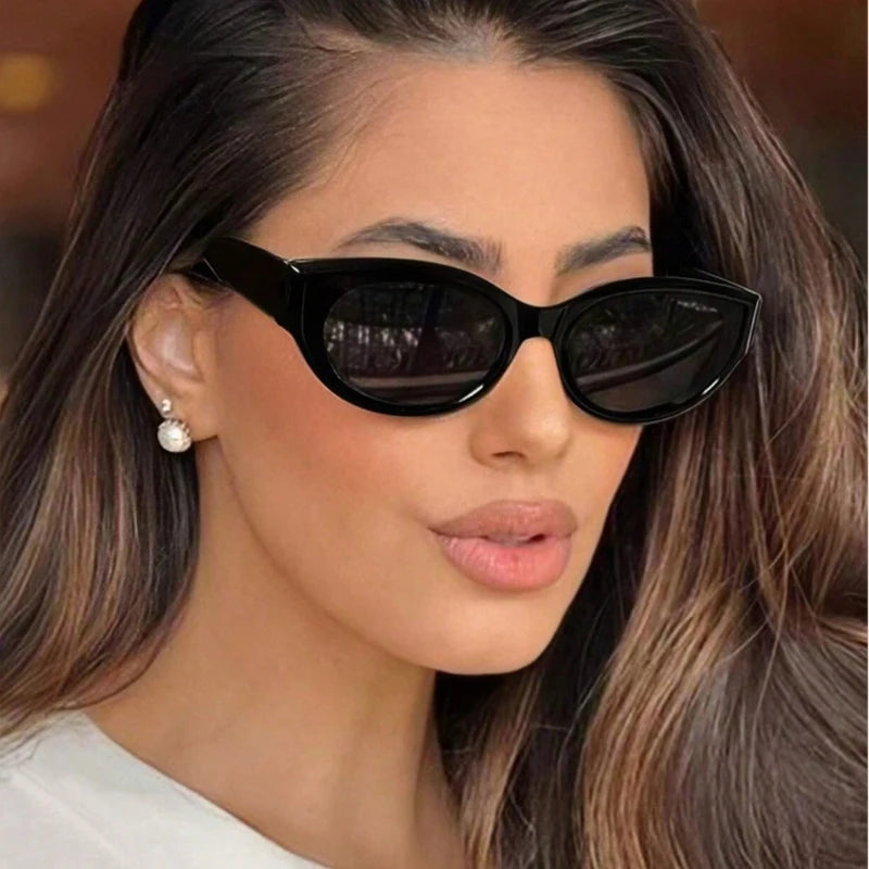 Black cat-eye sunglasses with a sleek upswept design, worn by a model with long, wavy hair and pearl earrings.