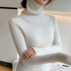 Slim-fit white cashmere turtleneck sweater with ribbed texture and high collar, shown worn with hands crossed at the wrists.