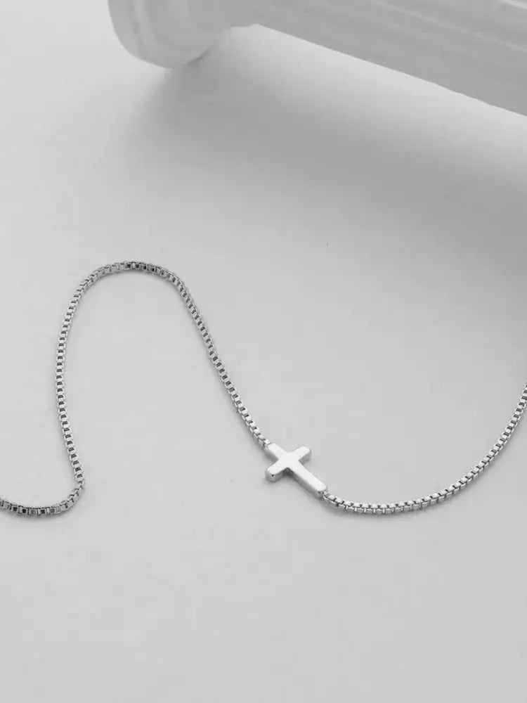 Silver high-polish mini cross pendant on a delicate chain, showcasing a minimalist design against a neutral background.