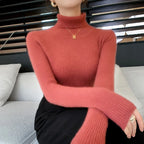 Slim-fit turtleneck sweater in a warm coral hue with ribbed texture, featuring a high collar and long sleeves.
