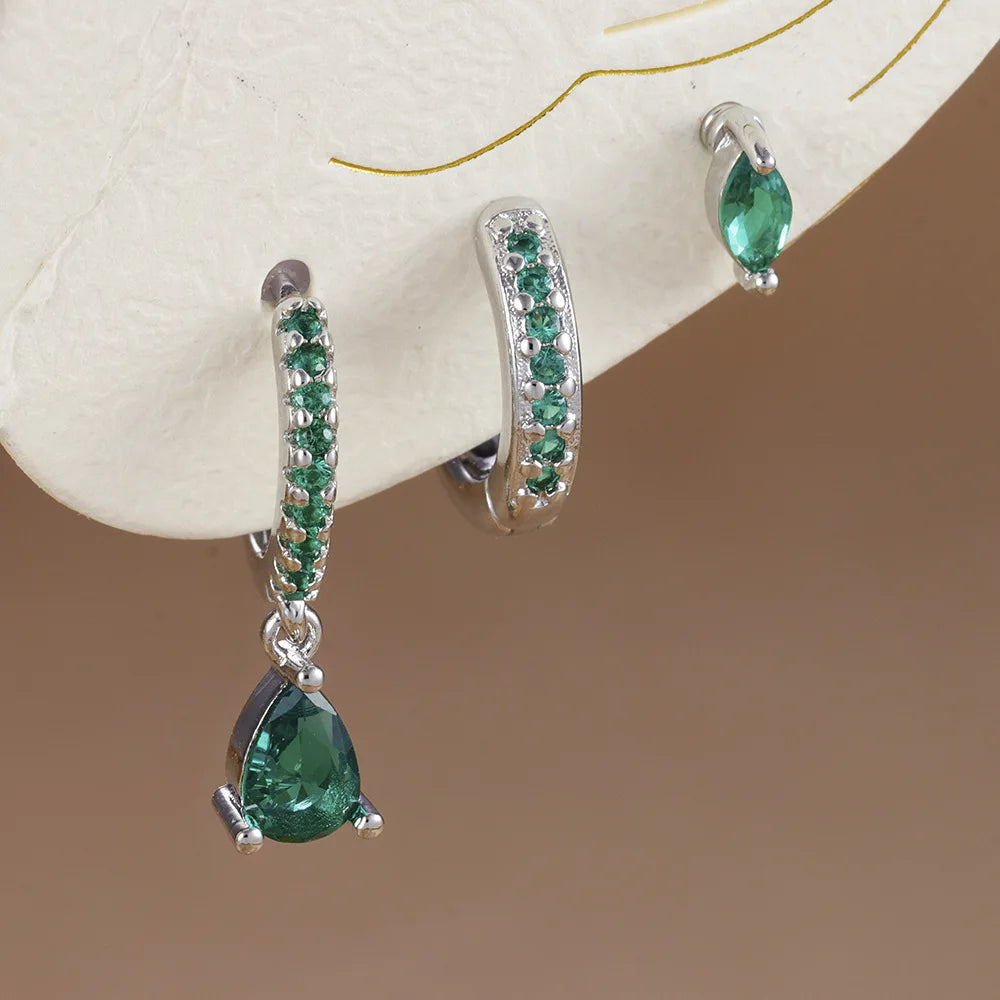 Three-piece earring set featuring metallic geometric designs with green accents, including a teardrop, hoops, and minimalist studs.