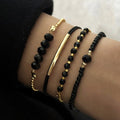 Four-piece bracelet set featuring shiny black onyx glass stones and gold-tone metallic beads, stacked on a wrist.