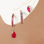 Three-piece earring set featuring shiny silver geometric designs, including a teardrop and two hoop styles, adorned with red stones.
